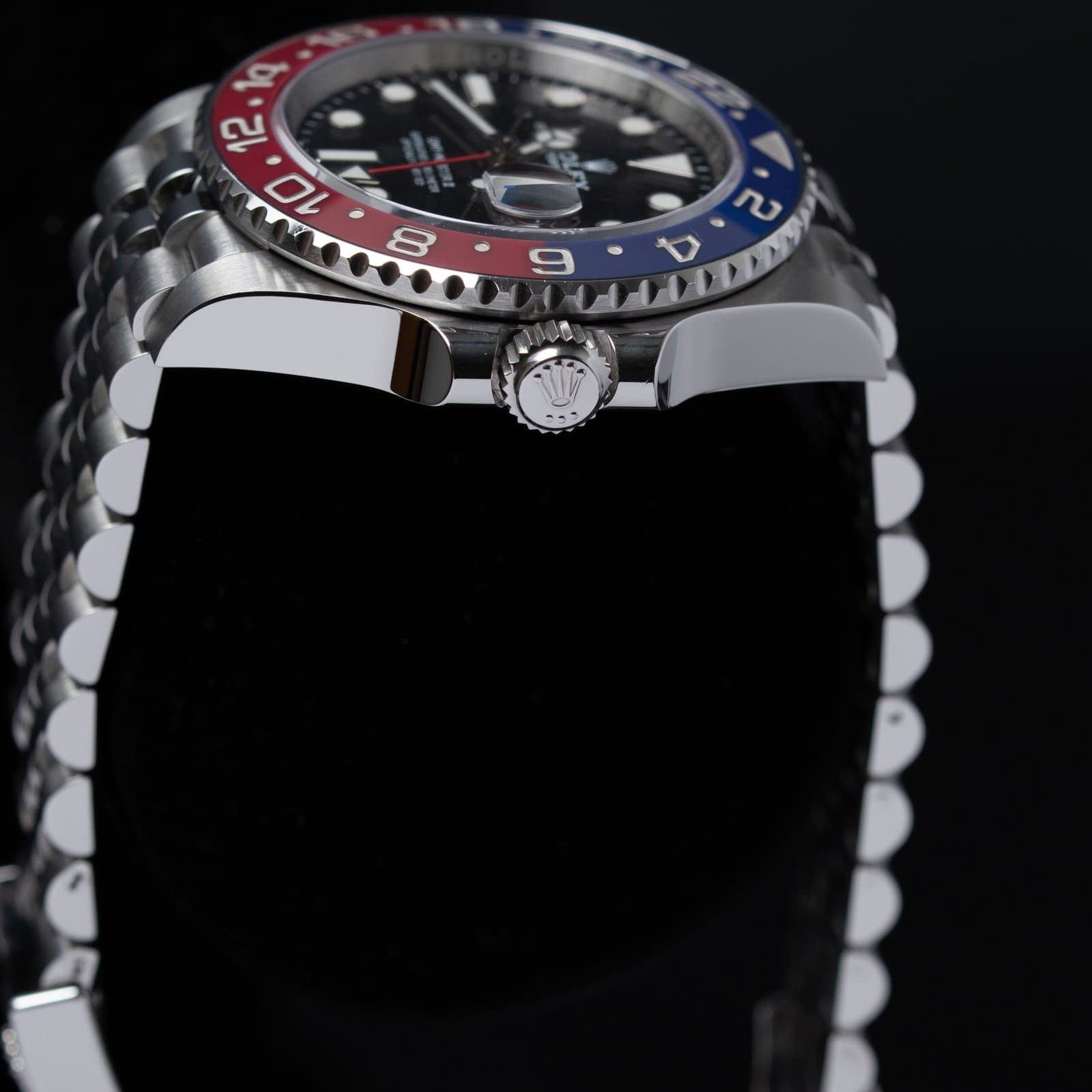 Steel Rolex GMT-Master II Pepsi with a red and blue bezel and black dial on a Jubilee bracelet, seen from the crown side on a black display cushion