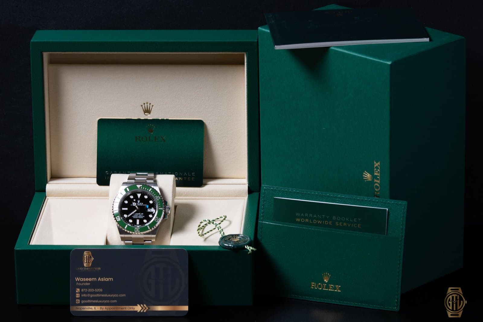 Steel Rolex Submariner Date 126610LV with a green bezel in its open green box, beside the warranty booklet, outer box and a Good Times Luxury business card reading Naperville, IL, By Appointment Only