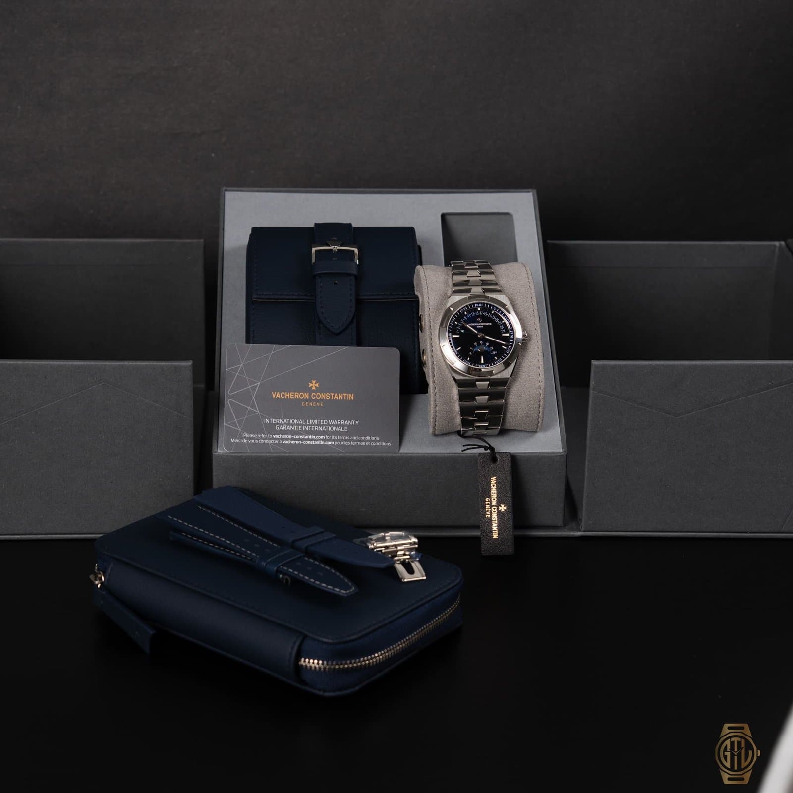 Steel Vacheron Constantin Overseas with a blue moon phase dial on its cushion in the open box, beside the warranty card, hang tag, a blue leather case and a zipped blue pouch holding a strap and a folding clasp