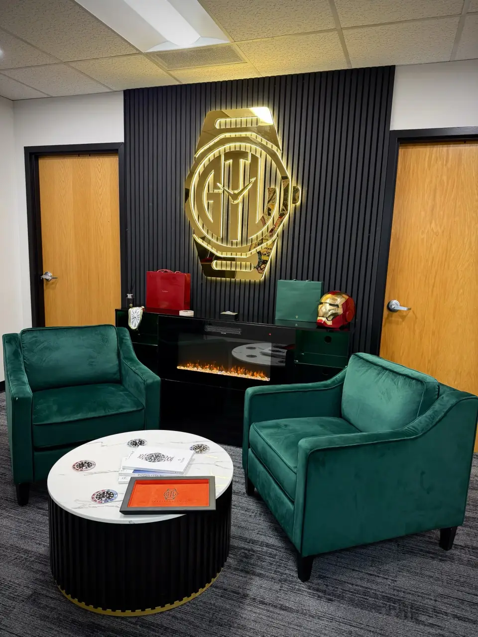 Waseem's private office suite: the lit GTL sign over a fireplace, two green velvet chairs and the orange GTL tray on the table