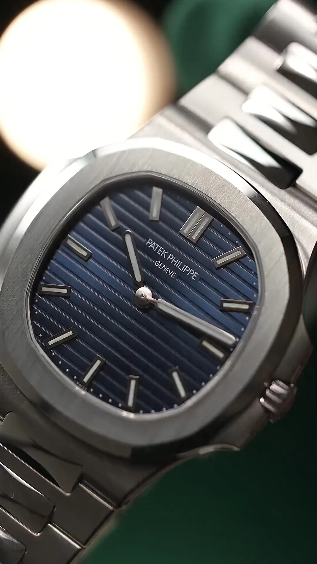 Illustrative film: a steel watch with a blue dial examined up close by gloved hands, ending on a cream pillow