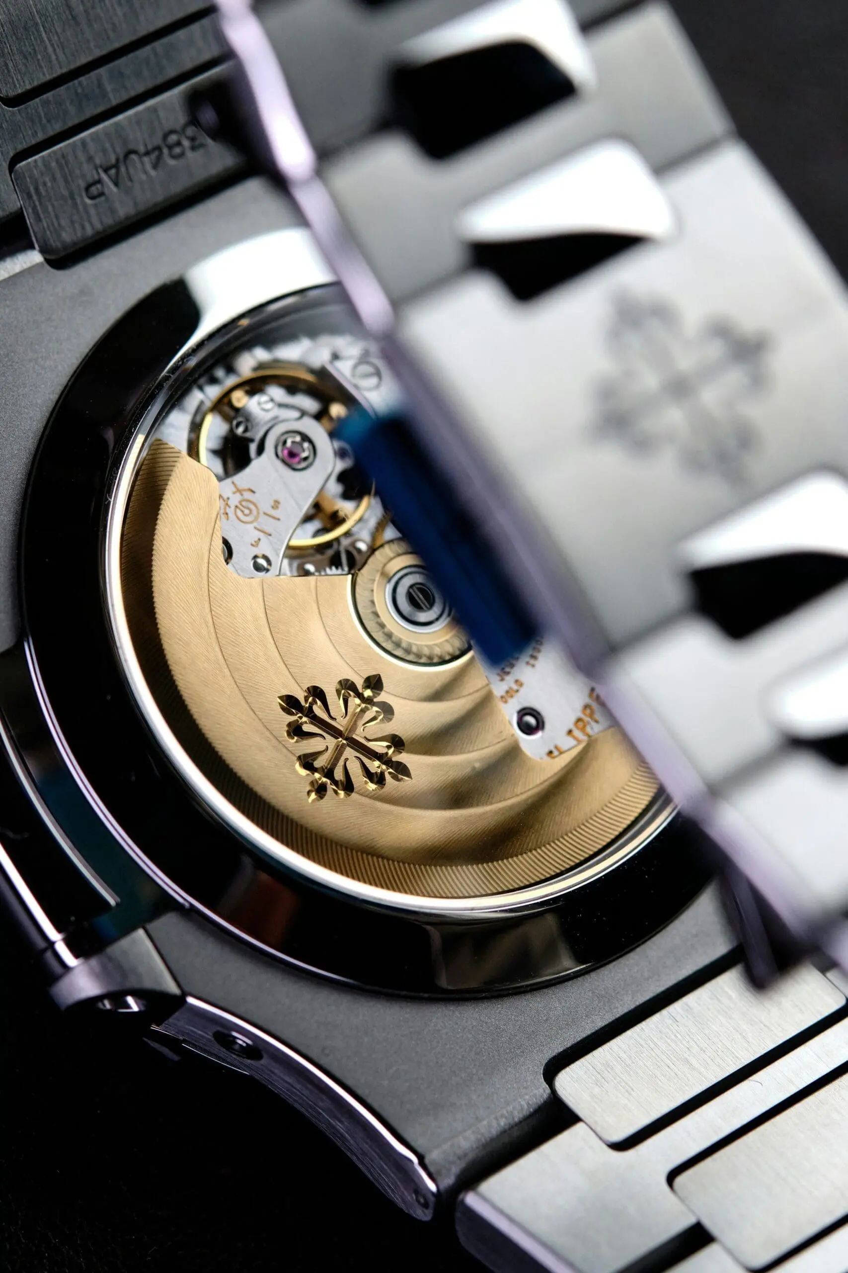 Close-up of a Patek Philippe watch movement through the exhibition caseback, showing the gold rotor with the Calatrava cross.