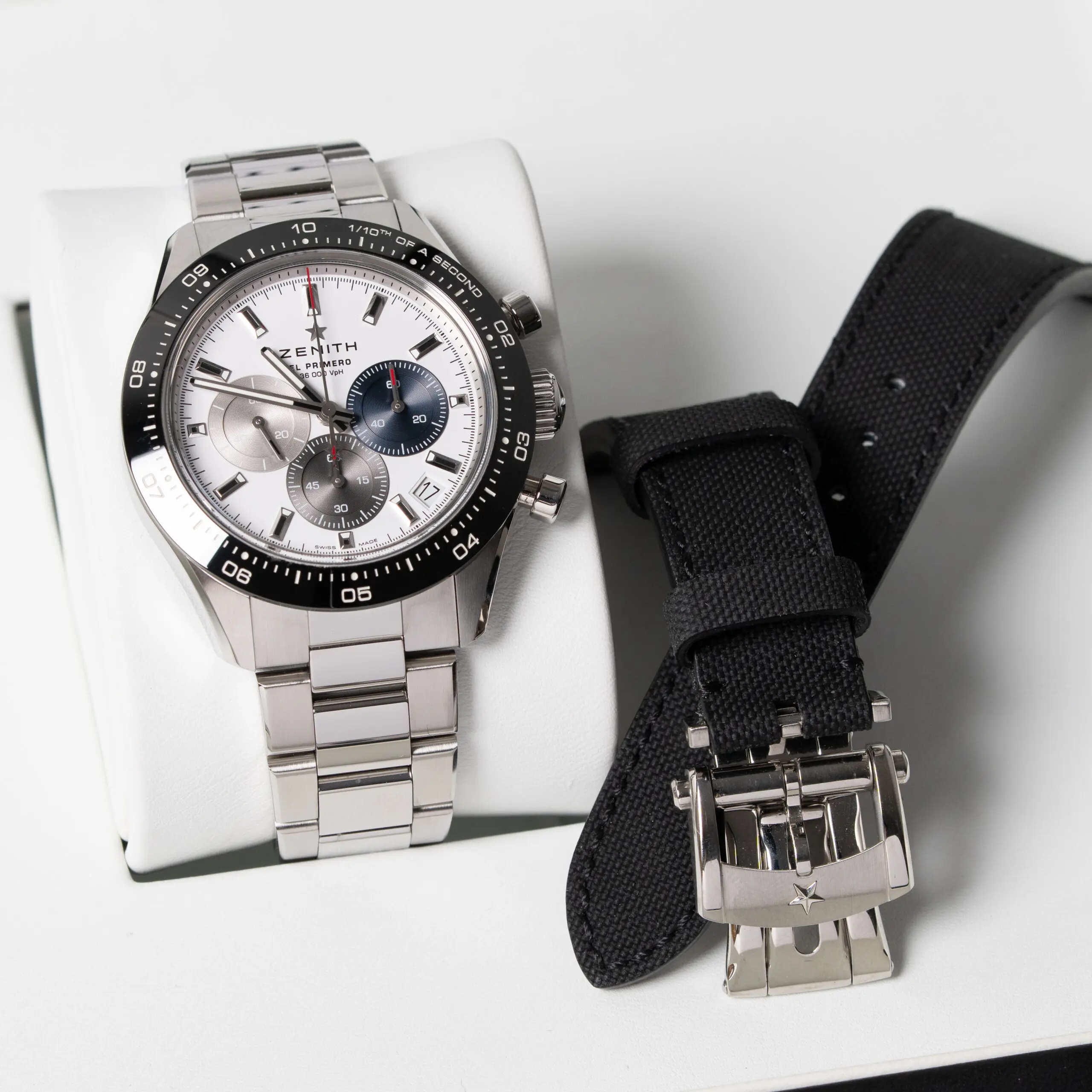 Stainless steel chronograph watch with black bezel and white dial photographed with extra strap
